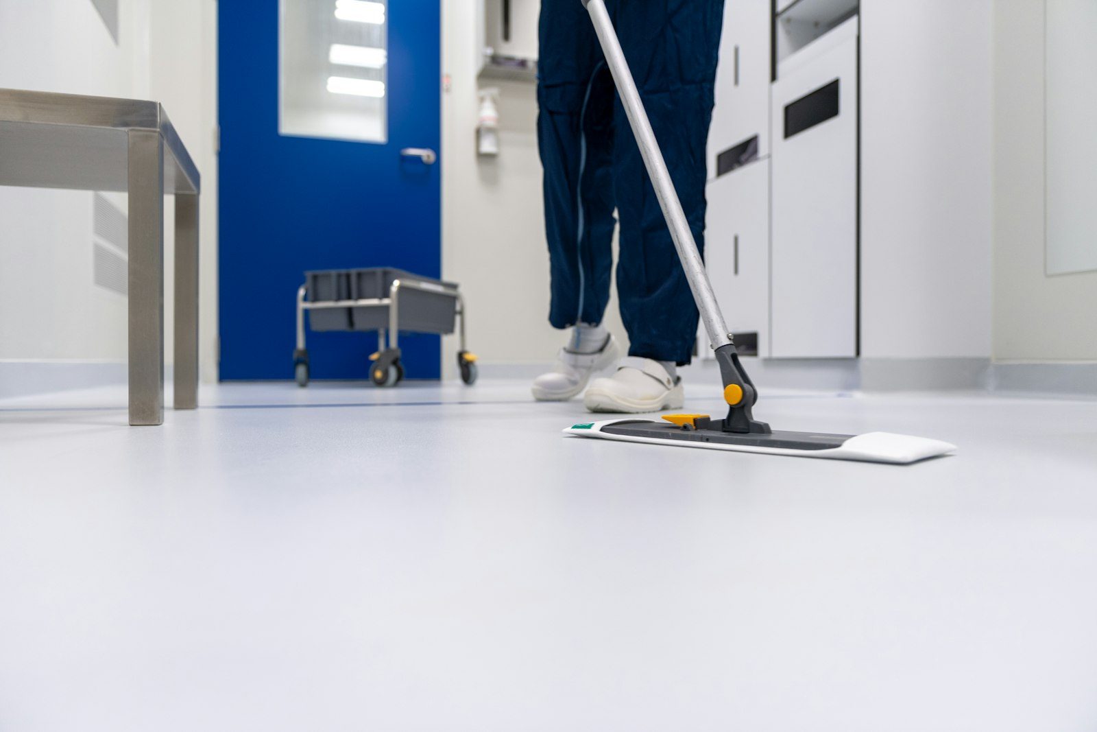 Cleaner in scrubs mopping a clinical corridor