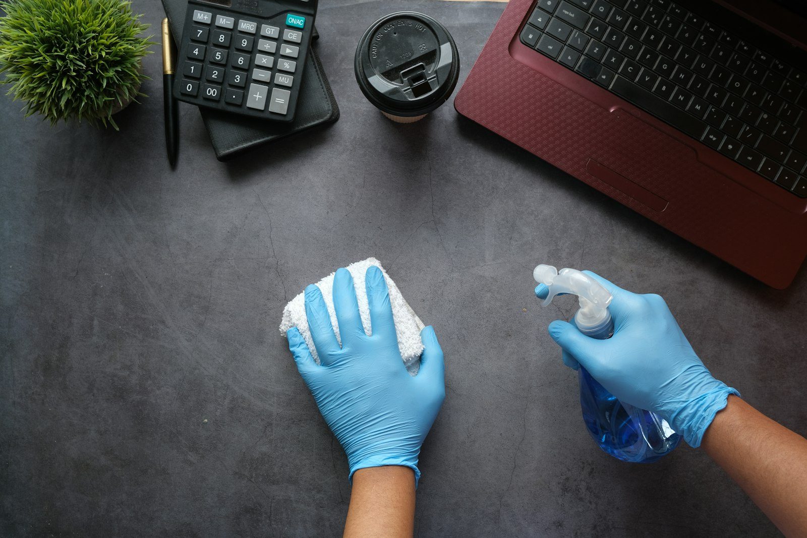 Cleaner in gloves wiping an office desk with spray and cloth